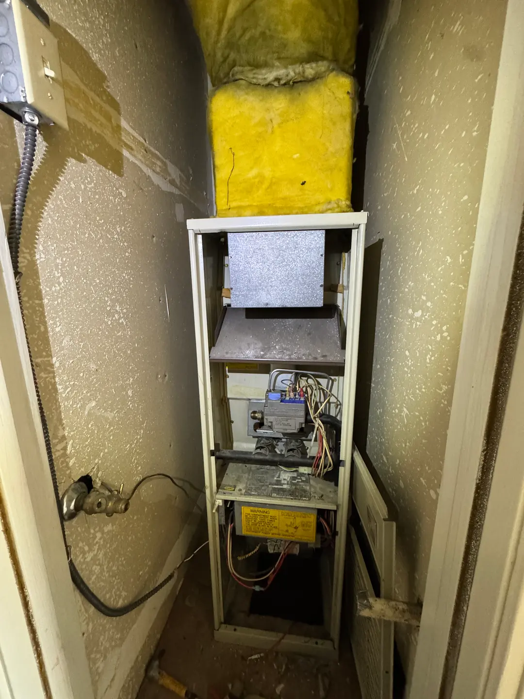 Aged residential gas furnace inside a dirty Westside Los Angeles closet showing dust-loaded burners, exposed wiring, and degraded insulation