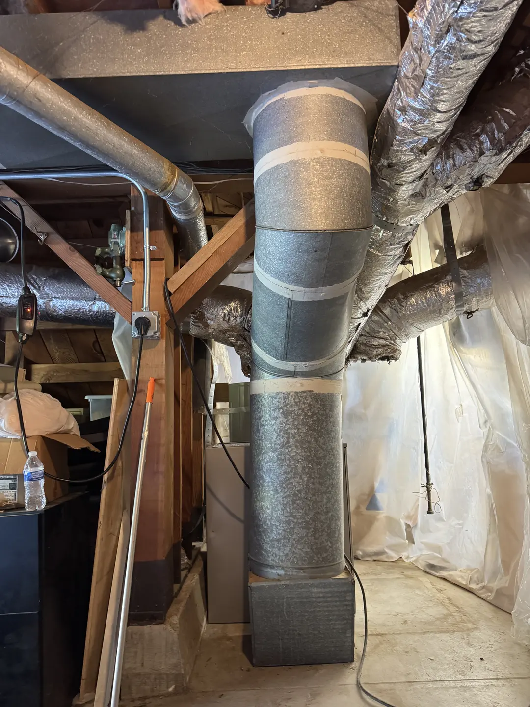 Large round galvanized supply duct and B-vent rising from the air handler in a West Los Angeles utility space during system replacement