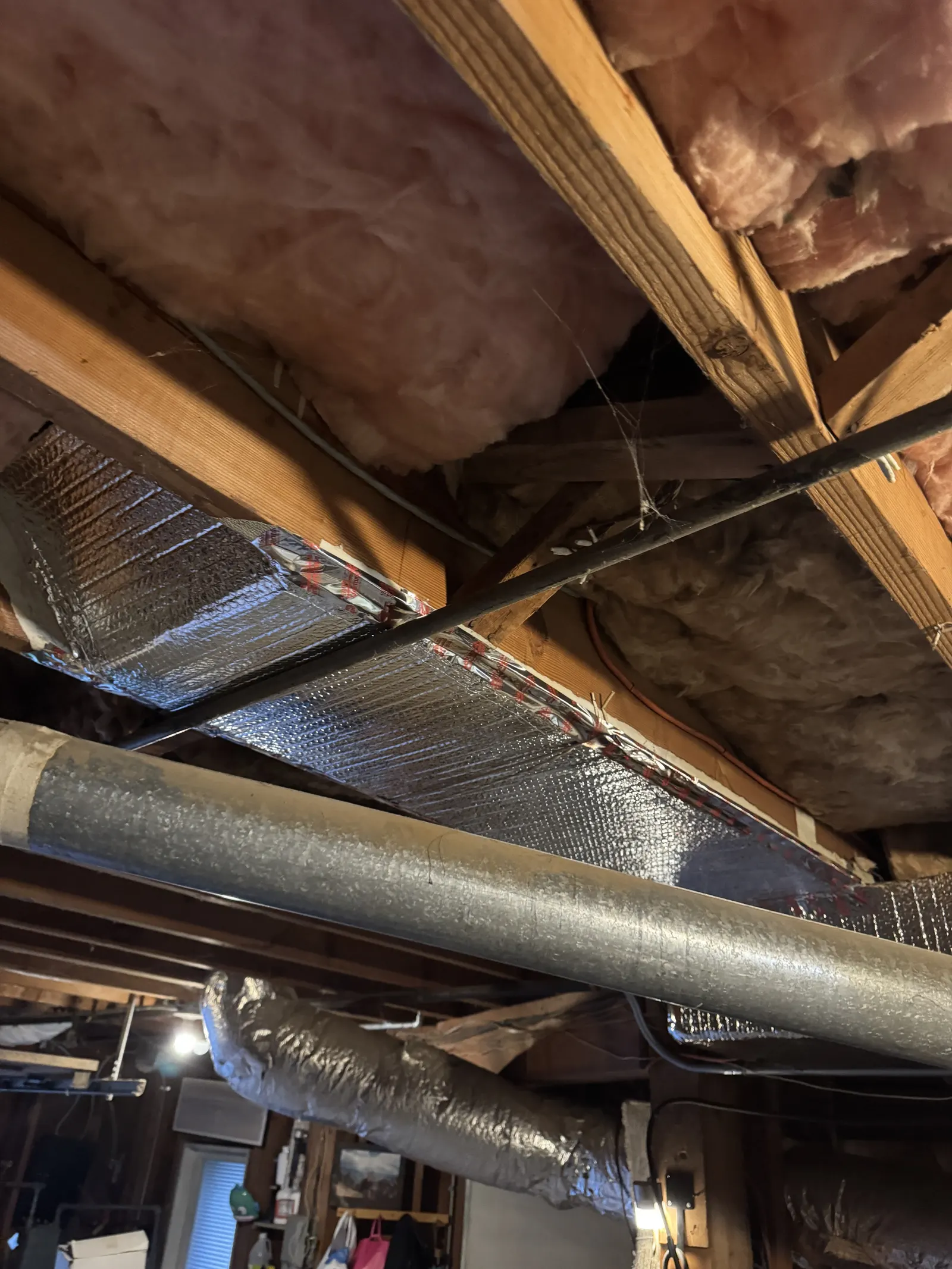 Insulated rectangular supply duct routed under fiberglass batt insulation in a West Los Angeles attic during HVAC retrofit