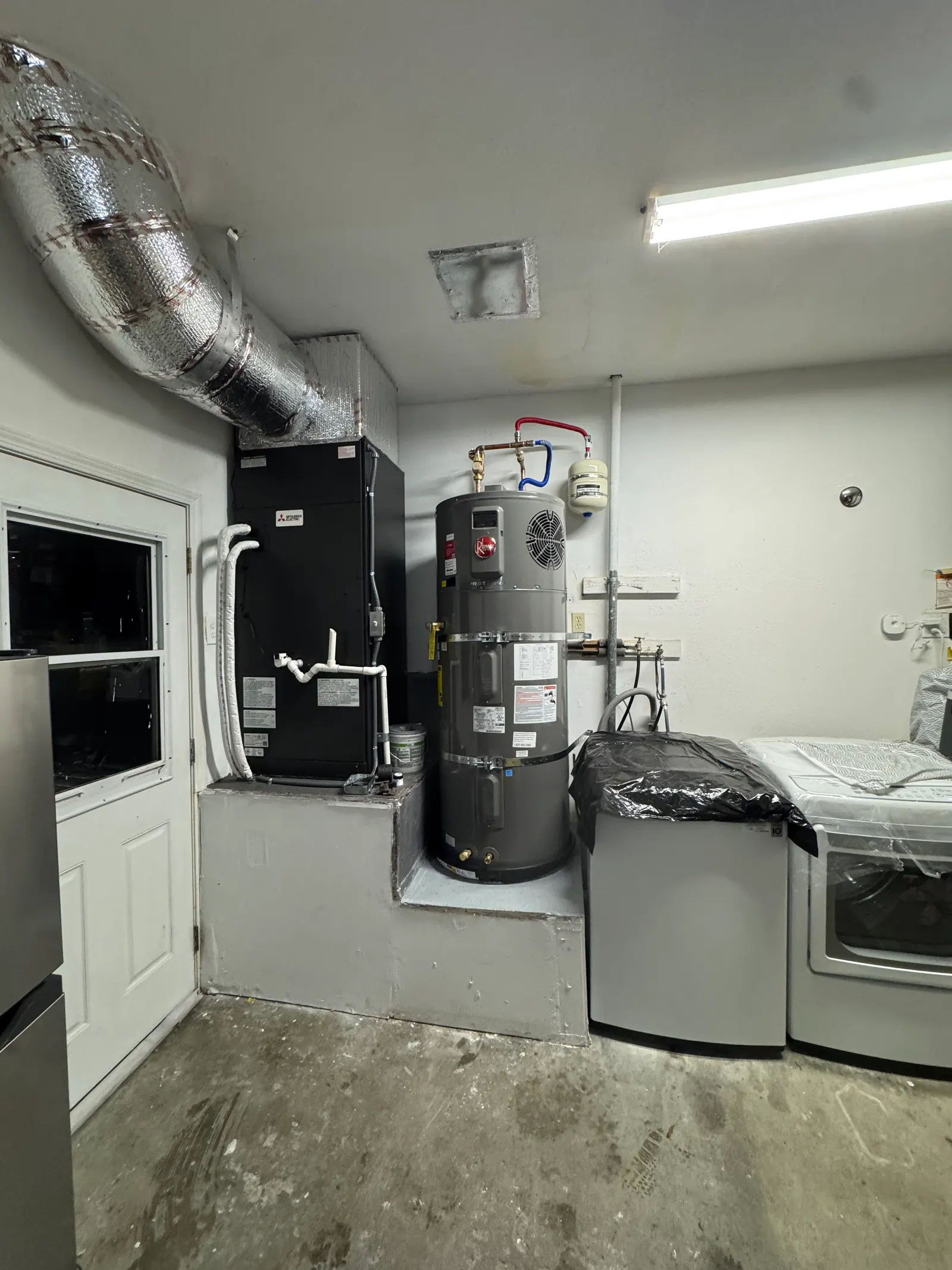 Rheem residential water heater installed alongside a Mitsubishi Electric air handler in a West Los Angeles garage utility room with insulated supply duct