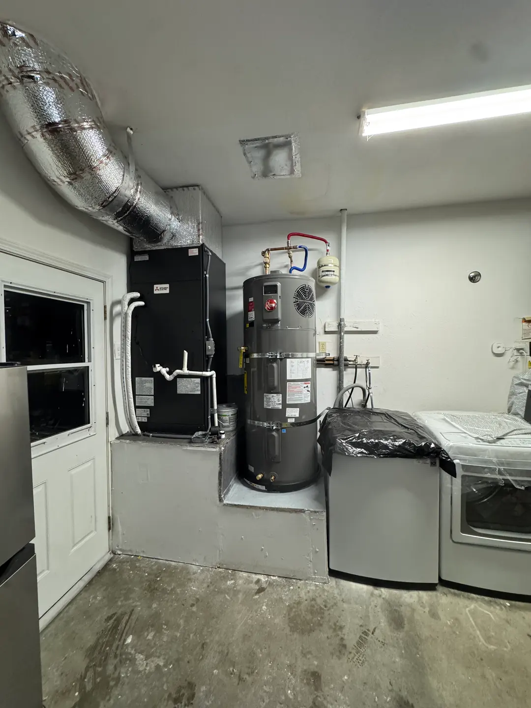 Rheem residential water heater installed alongside a Mitsubishi Electric air handler in a West Los Angeles garage utility room with insulated supply duct