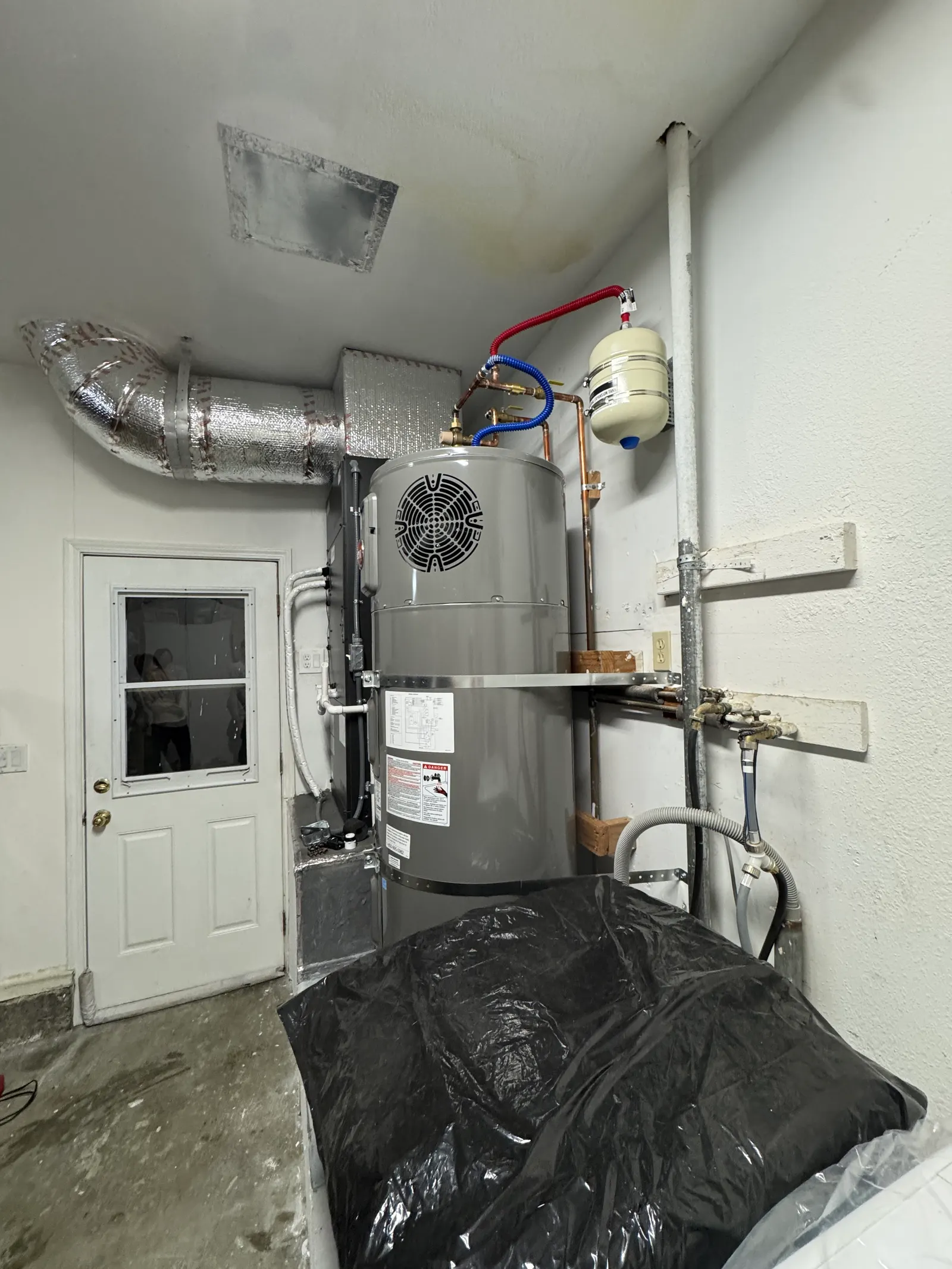 Rheem water heater installed beside a Mitsubishi Electric air handler in a clean white-walled mechanical room with PVC condensate piping and dedicated drain pan