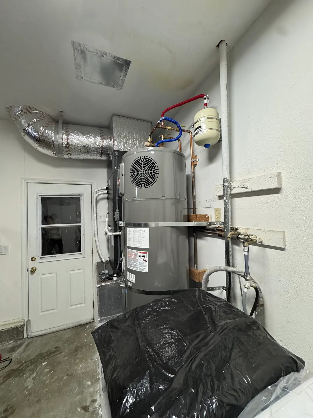 Rheem water heater installed beside a Mitsubishi Electric air handler in a clean white-walled mechanical room with PVC condensate piping and dedicated drain pan