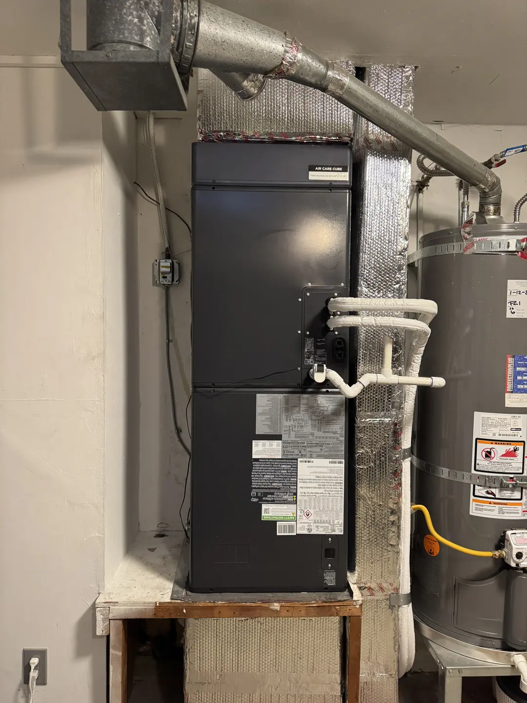 Black multi-position air handler tied into supply plenum in a Pico-Robertson mechanical closet next to a 50-gallon water heater