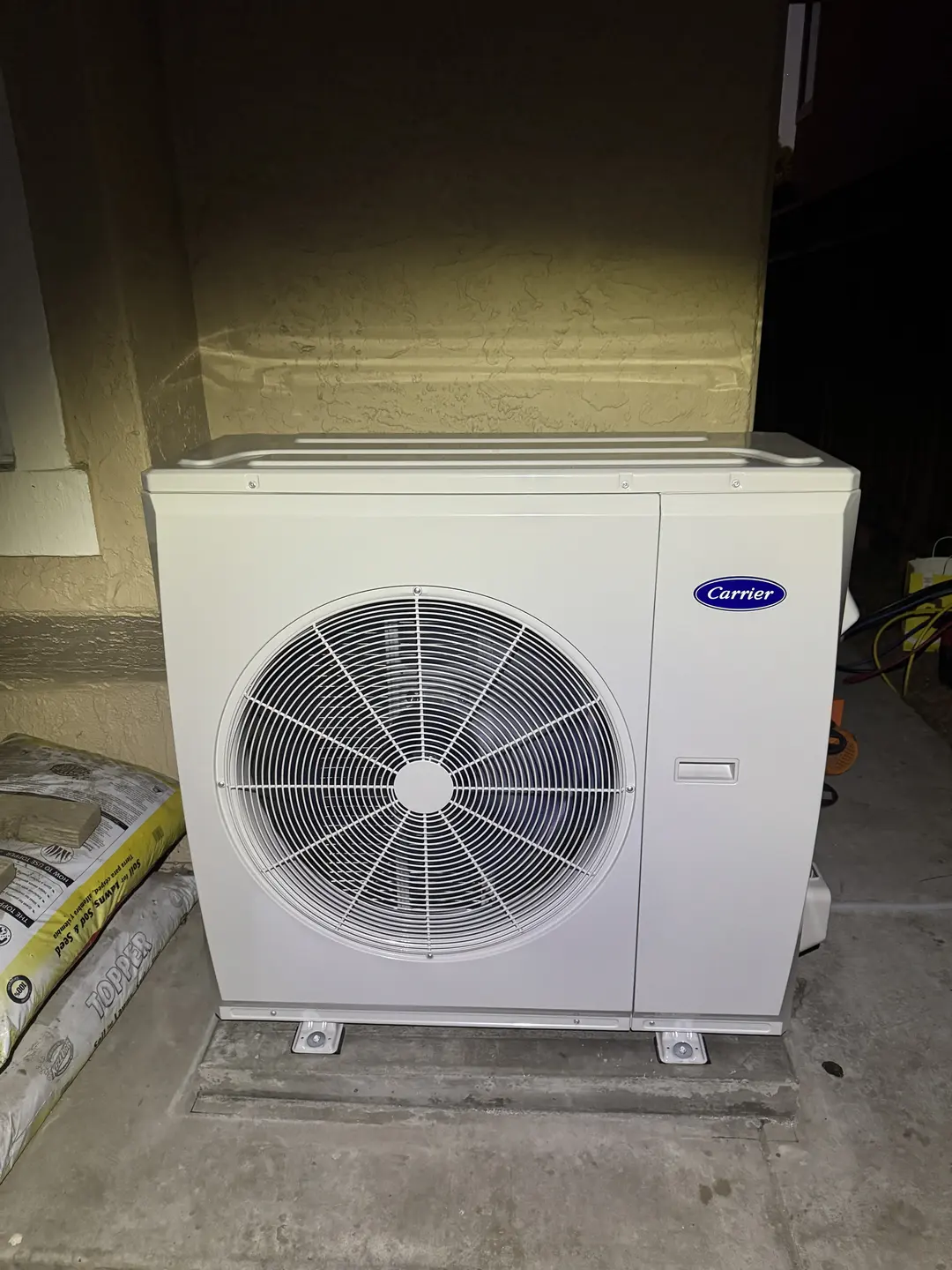 Carrier inverter heat pump outdoor unit installed on a stucco wall pad in a West LA side yard, ready for line-set hookup